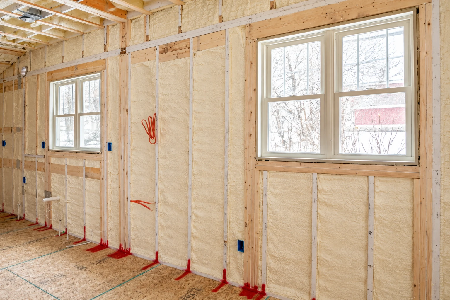 Spray foam insulation fills the wall framing around two windows in an unfinished room.